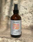 Bottle of Petal Woods Aromatic Body Oil by banyo on a natural stone surface with blurred tree background