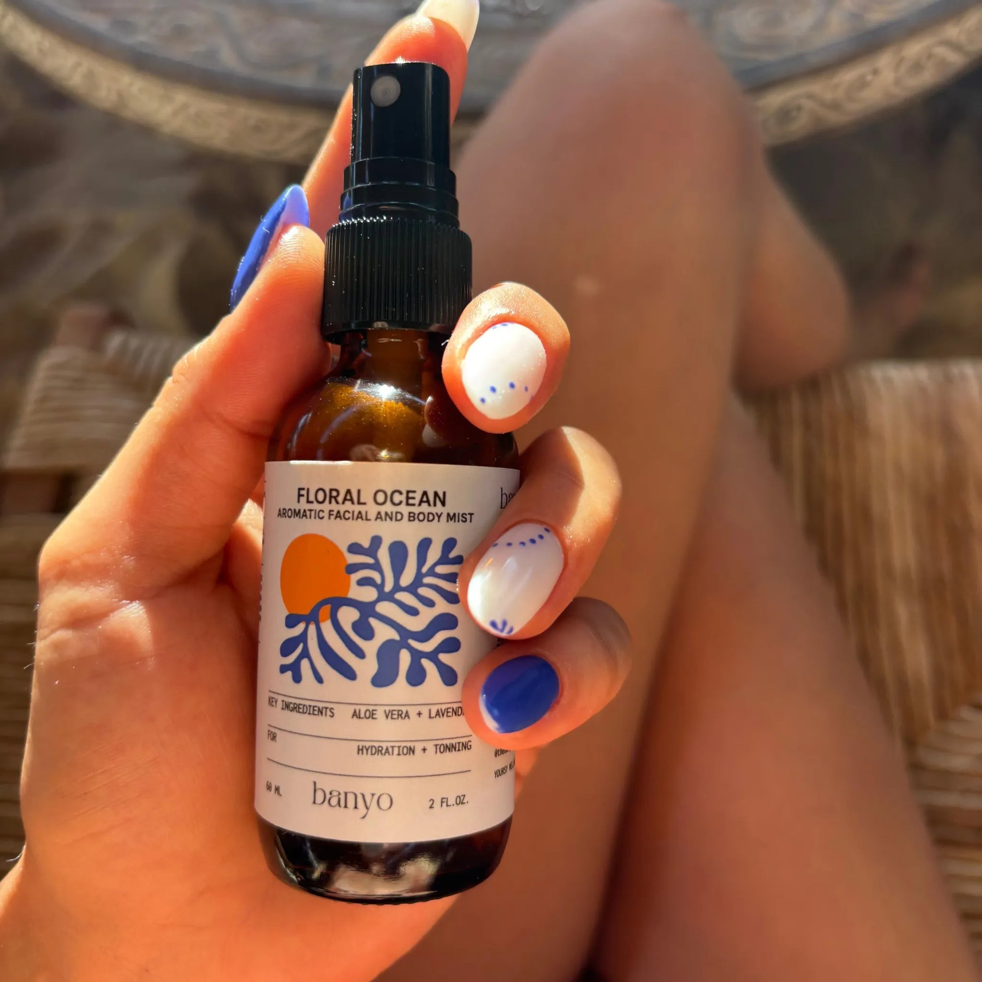 Hand holding a bottle of 'Floral Ocean' mist by banyo with a blurred background