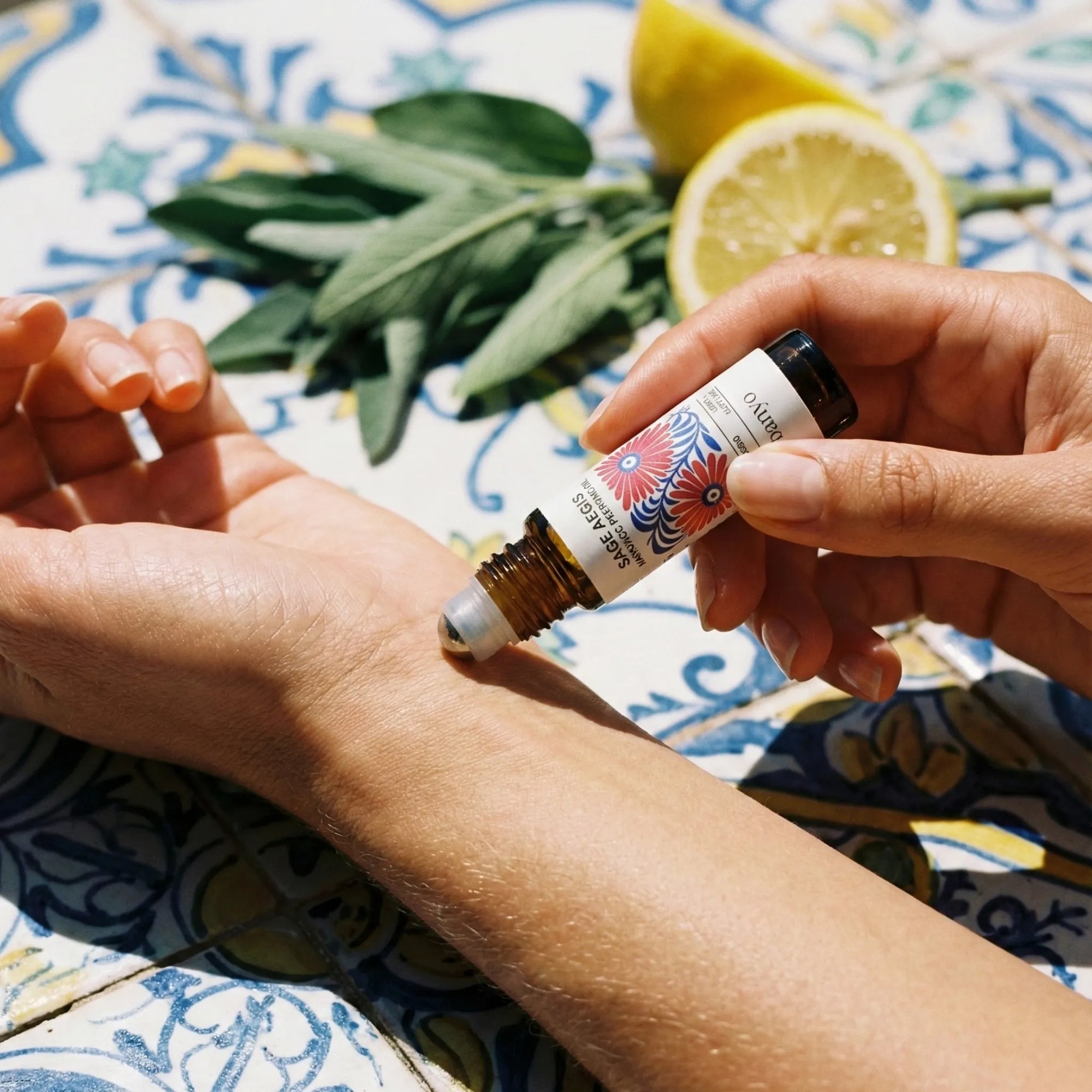 Person applying essential oil to wrist with lemons and herbs on a patterned fabric background