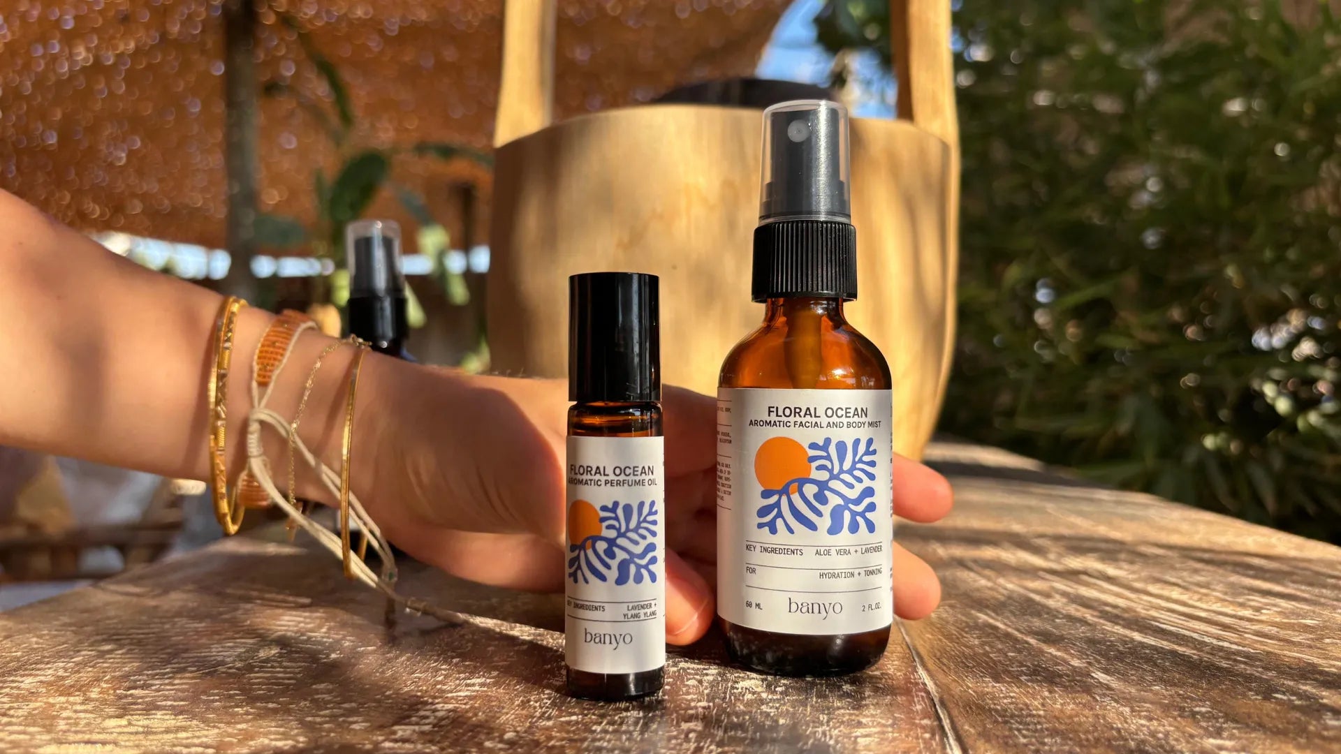 Hand holding three bottles of 'Floral Ocean' products on a wooden surface with a blurred natural background.