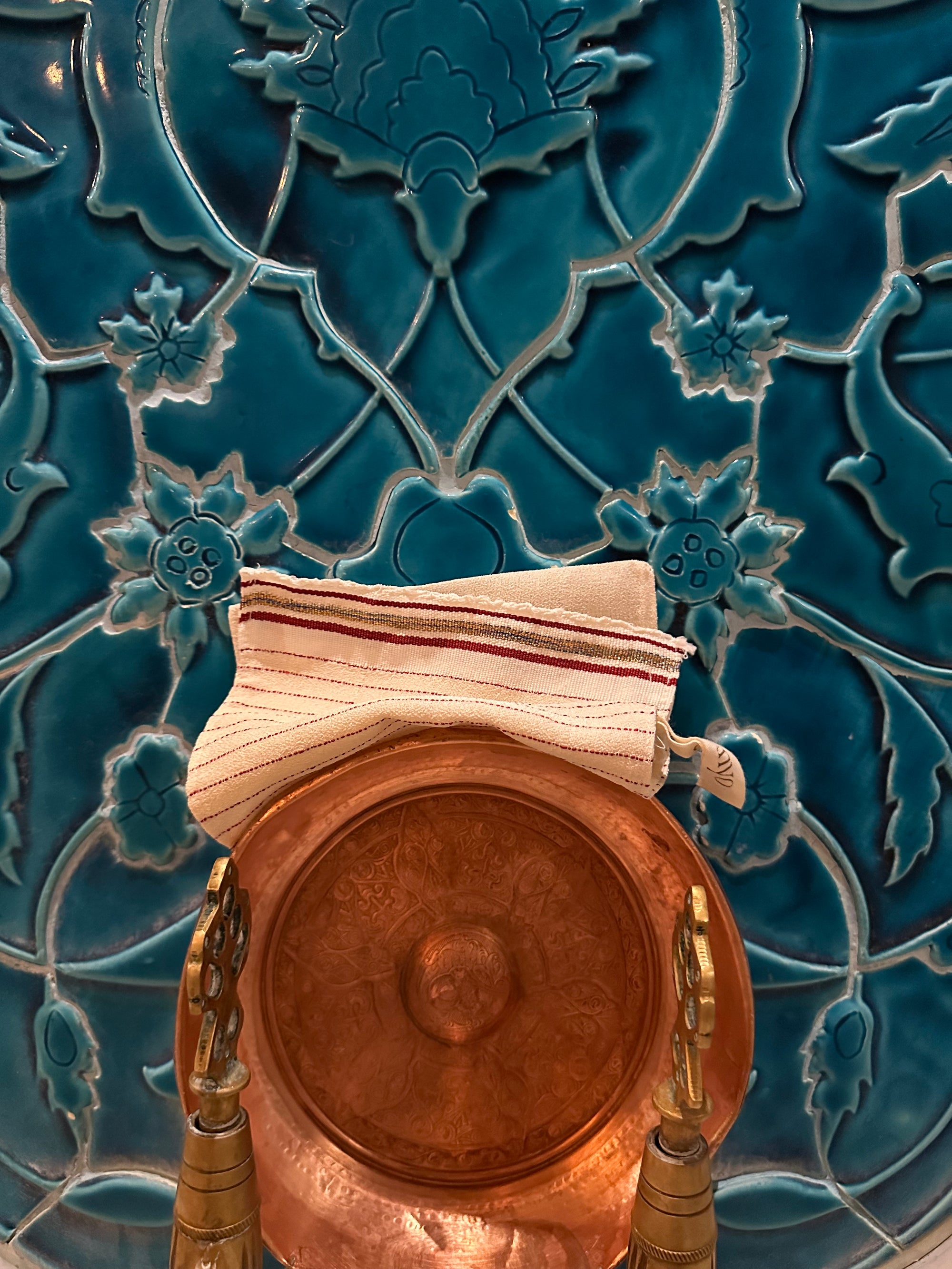 Copper pot with striped bath cloth on a blue tiled wall